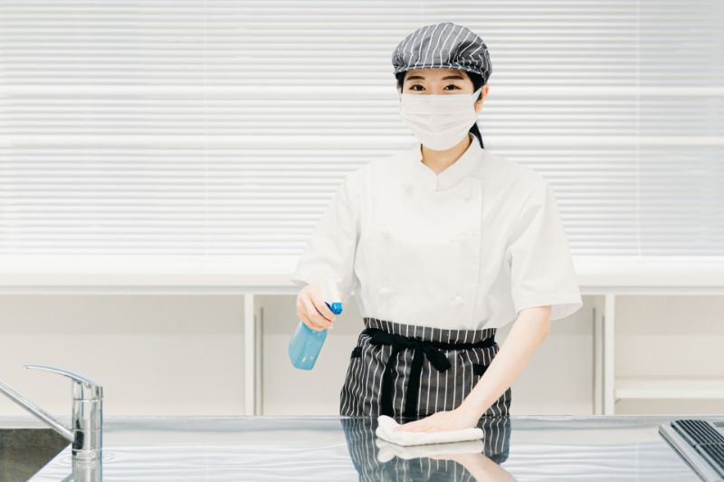 コックコート姿でキッチンを除菌する女性