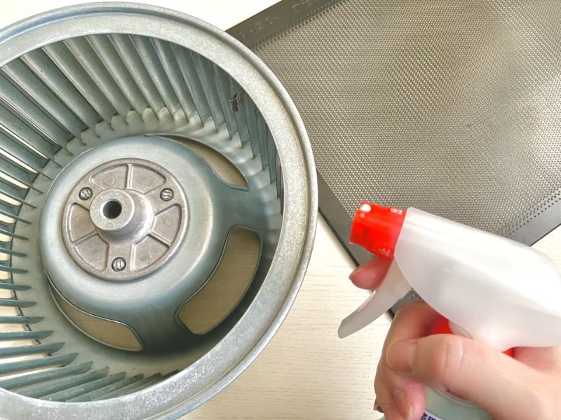 換気扇のシロッコファンに洗剤をスプレーして掃除する様子(イメージ写真)